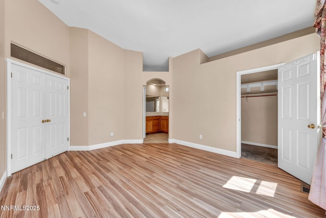 7449 Ambush Cir, Sparks, NV 89436 - unfurnished bedroom with a closet, light wood-style flooring, arched walkways, connected bathroom, and a walk in closet