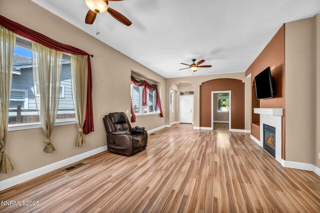 7449 Ambush Cir, Sparks, NV 89436 - unfurnished living room featuring ceiling fan, arched walkways, a glass covered fireplace, and light wood-style floors