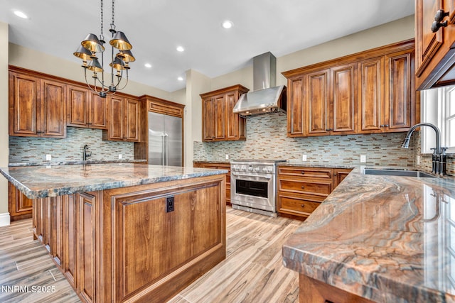 6145 Triple Crown Dr, Reno, NV 89511 - kitchen with premium appliances, wall chimney range hood, brown cabinets, a kitchen island, and light wood-type flooring
