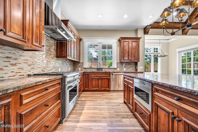 6145 Triple Crown Dr, Reno, NV 89511 - kitchen featuring a chandelier, wall chimney range hood, appliances with stainless steel finishes, dark stone counters, and light wood finished floors