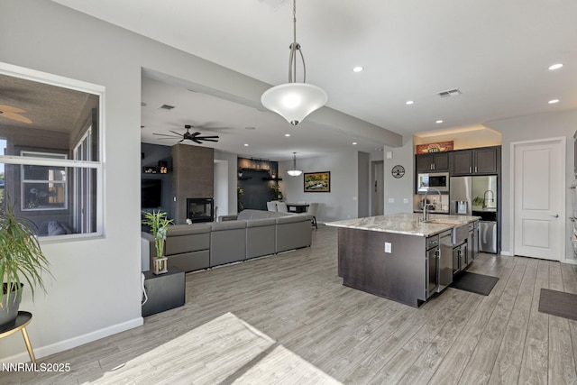 9435 Stony Hill Rd, Reno, NV 89521 - kitchen featuring stainless steel appliances, light wood-type flooring, dark brown cabinets, light stone countertops, and an island with sink