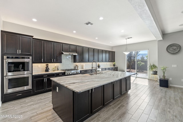 9435 Stony Hill Rd, Reno, NV 89521 - kitchen featuring appliances with stainless steel finishes, under cabinet range hood, backsplash, light wood-style flooring, and light stone counters