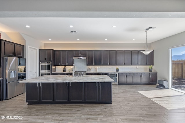 9435 Stony Hill Rd, Reno, NV 89521 - kitchen with beverage cooler, appliances with stainless steel finishes, tasteful backsplash, light wood-style flooring, and a kitchen island with sink