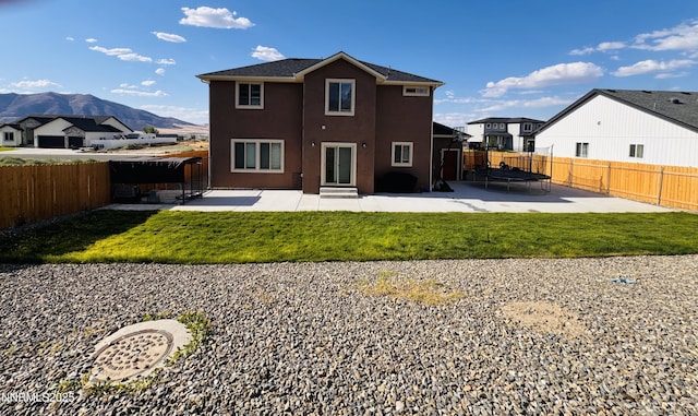5290 Marla Dr, Winnemucca, NV 89445 - back of property with a trampoline, a patio, a fenced backyard, a mountain view, and stucco siding