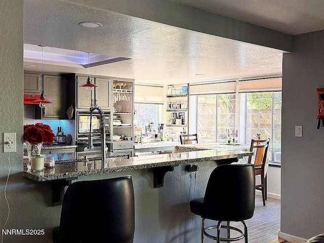 6673 Enchanted Valley Dr, Reno, NV 89523 - kitchen featuring a breakfast bar, dark stone counters, hanging light fixtures, backsplash, and a textured ceiling