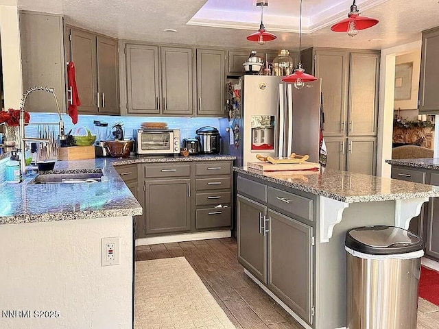 6673 Enchanted Valley Dr, Reno, NV 89523 - kitchen with stainless steel fridge with ice dispenser, gray cabinetry, dark wood finished floors, and hanging light fixtures