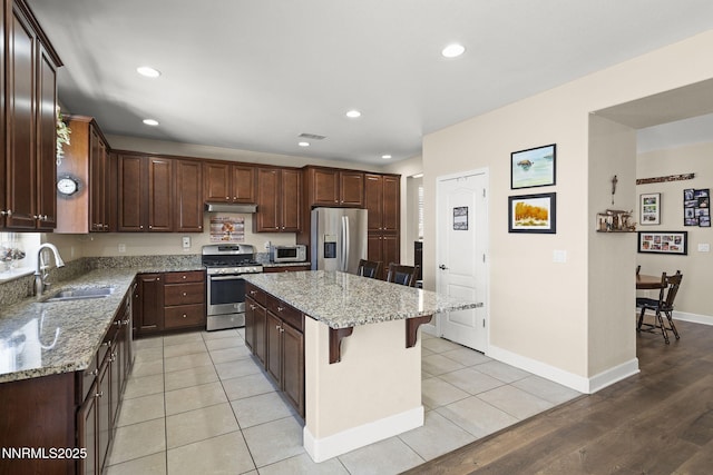 10125 Mesa Cortona Dr, Reno, NV 89521 - kitchen featuring stainless steel appliances, under cabinet range hood, a breakfast bar area, a center island, and light stone countertops