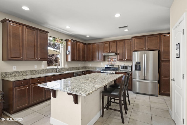 10125 Mesa Cortona Dr, Reno, NV 89521 - kitchen featuring appliances with stainless steel finishes, under cabinet range hood, a center island, light tile patterned floors, and a breakfast bar