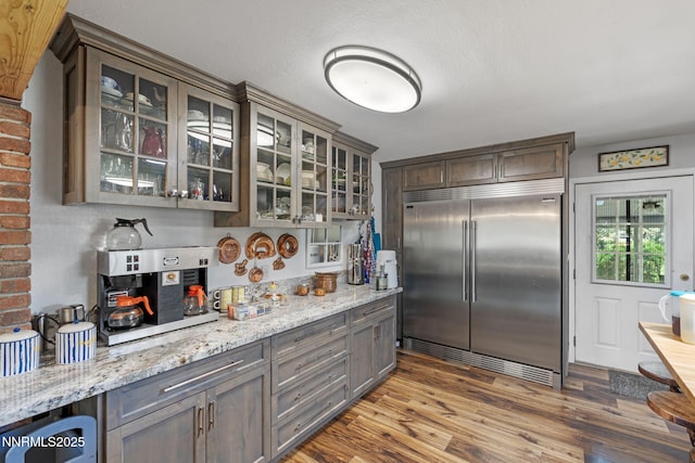 2450 Chukar Dr, Washoe Valley, NV 89704 - kitchen with built in fridge, wood finished floors, glass insert cabinets, and light stone countertops