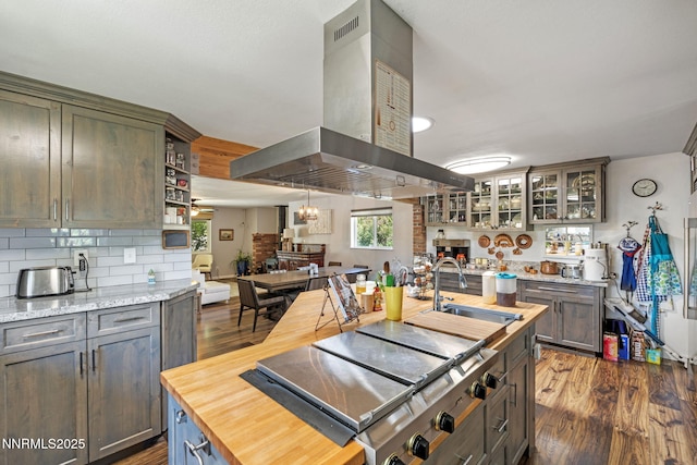 2450 Chukar Dr, Washoe Valley, NV 89704 - kitchen with wall chimney range hood, cooktop, wooden counters, an island with sink, and tasteful backsplash