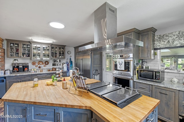 2450 Chukar Dr, Washoe Valley, NV 89704 - kitchen with wood counters, wall chimney exhaust hood, stainless steel appliances, a center island, and glass insert cabinets