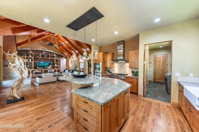 48 Rose Creek Ln, Reno, NV 89511 - kitchen featuring wall chimney range hood, light wood-style flooring, a kitchen island with sink, light stone counters, and hanging light fixtures