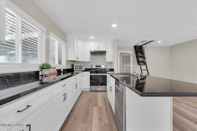 1094 Johnson Blvd, South Lake Tahoe, CA 96150 - kitchen featuring appliances with stainless steel finishes, range hood, light wood-style floors, a kitchen island with sink, and white cabinets