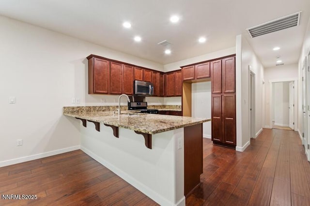 1460 Waterloo Dr, Reno, NV 89509 - kitchen with stainless steel appliances, a peninsula, light stone counters, dark wood-style flooring, and a kitchen breakfast bar
