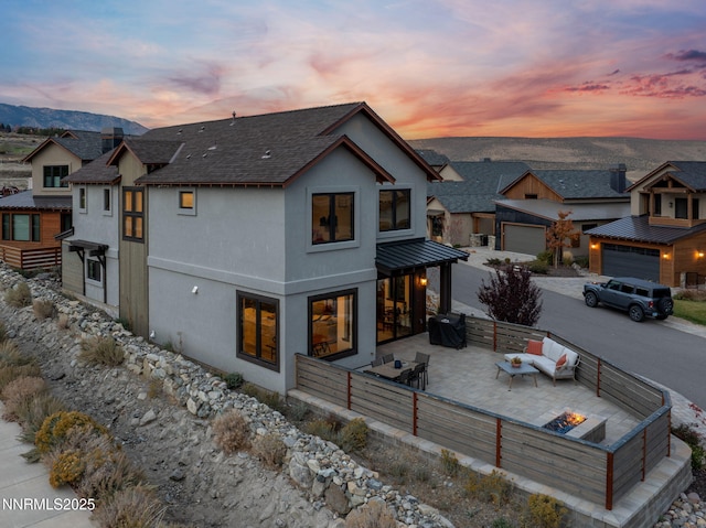 2912 Portrush Dr, Genoa, NV 89411 - back of property at dusk featuring an outdoor living space with a fire pit, a shingled roof, stucco siding, a patio area, and driveway
