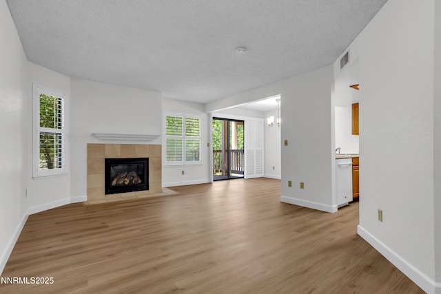 2875 Idlewild Dr Apt 5, Reno, NV 89509 - unfurnished living room with a chandelier, a tiled fireplace, light wood-type flooring, healthy amount of natural light, and a textured ceiling