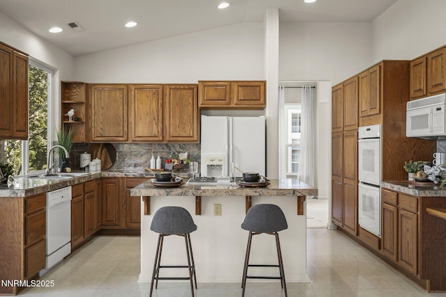 4811 Elkcreek Trl, Reno, NV 89519 - kitchen featuring white appliances, lofted ceiling, a center island, brown cabinetry, and decorative backsplash