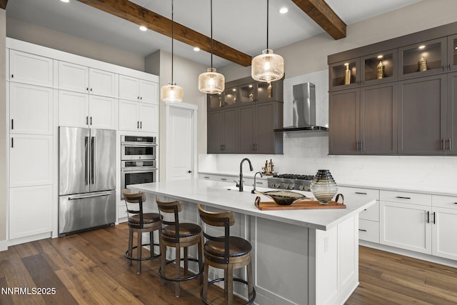 6122 S Pleasant Oak Trl, Reno, NV 89511 - kitchen with stainless steel appliances, wall chimney exhaust hood, dark wood-style flooring, beamed ceiling, and glass insert cabinets