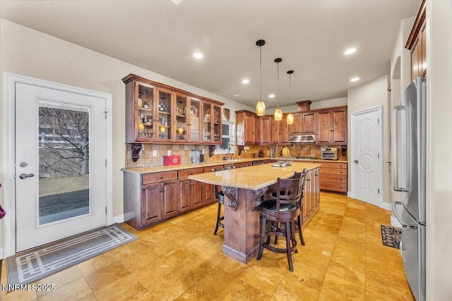 1962 Comstock Dr, Gardnerville, NV 89410 - kitchen featuring freestanding refrigerator, under cabinet range hood, a kitchen island, backsplash, and a kitchen bar