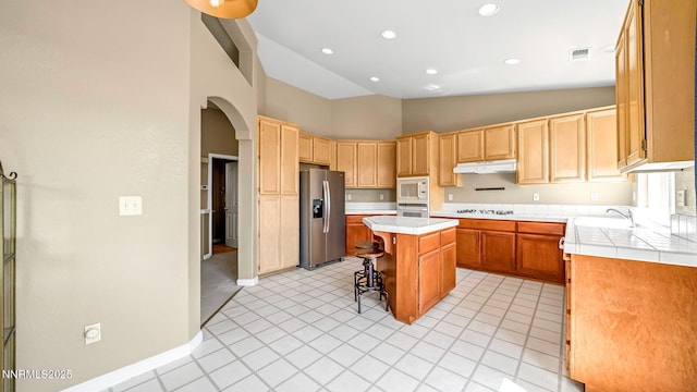 7302 Little Easy St, Sparks, NV 89436 - kitchen featuring arched walkways, tile countertops, a center island, a kitchen breakfast bar, and stainless steel refrigerator with ice dispenser