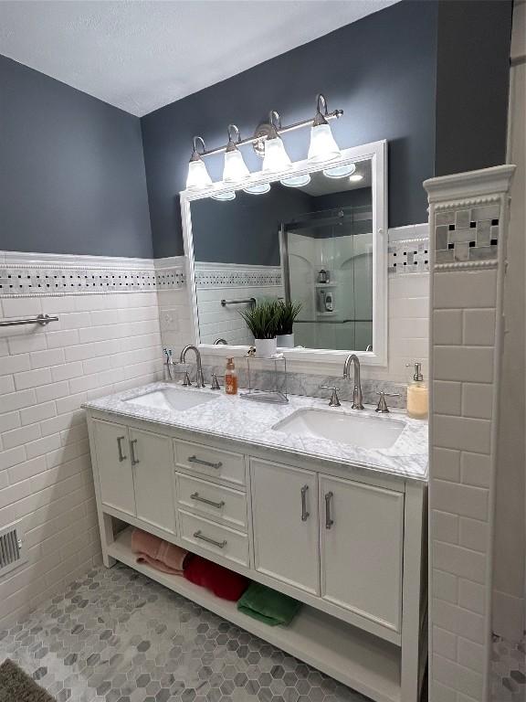 563 W 9th St, Erie, PA 16502 - bathroom with tile walls, double vanity, a shower stall, wainscoting, and tile patterned floors