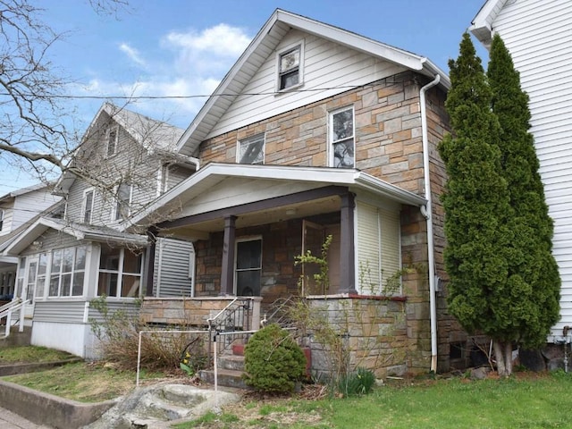 view of front of home featuring a sunroom, stone siding, and covered porch
