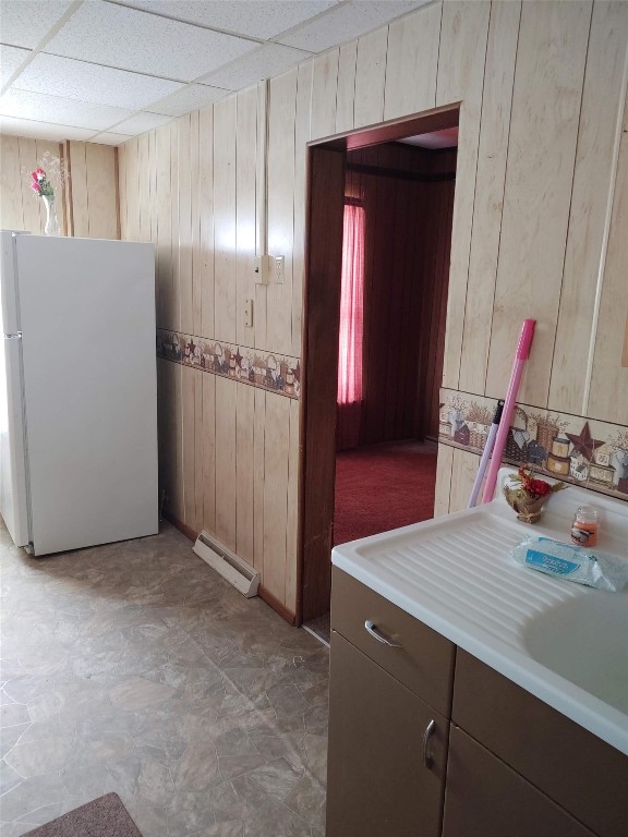 interior space with baseboard heating, wooden walls, a drop ceiling, and vanity