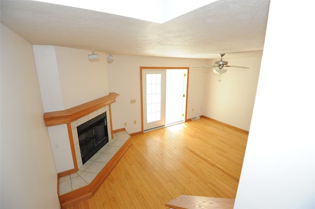 unfurnished living room featuring a tiled fireplace, ceiling fan, a textured ceiling, and light wood-type flooring