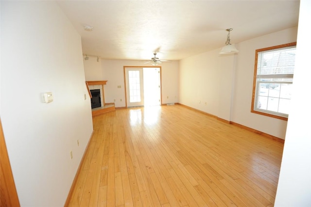 unfurnished living room featuring a tile fireplace, a healthy amount of sunlight, and light wood-type flooring