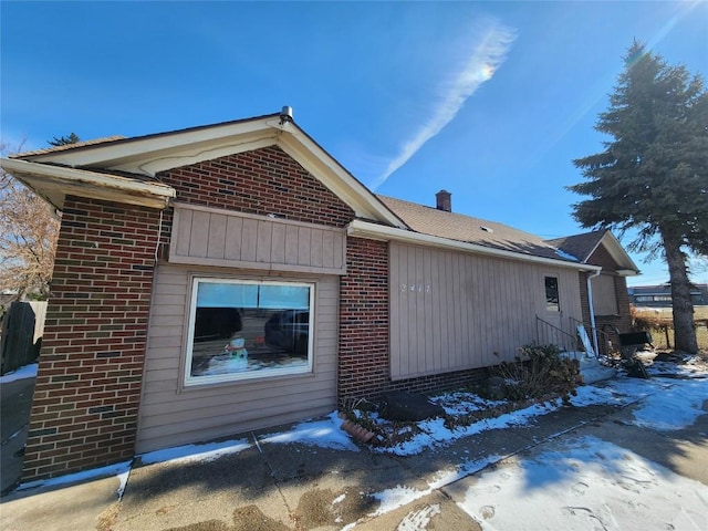 view of side of home with entry steps, brick siding, and a chimney