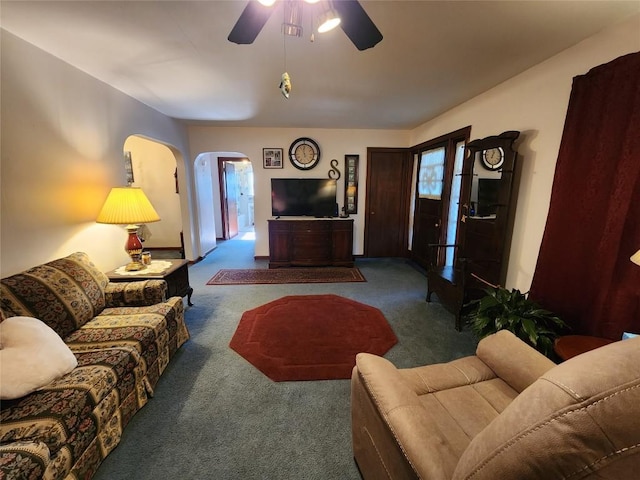 living area featuring arched walkways, carpet floors, and a ceiling fan