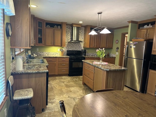 kitchen featuring gas stove, stainless steel refrigerator, wall chimney exhaust hood, decorative light fixtures, and a kitchen island