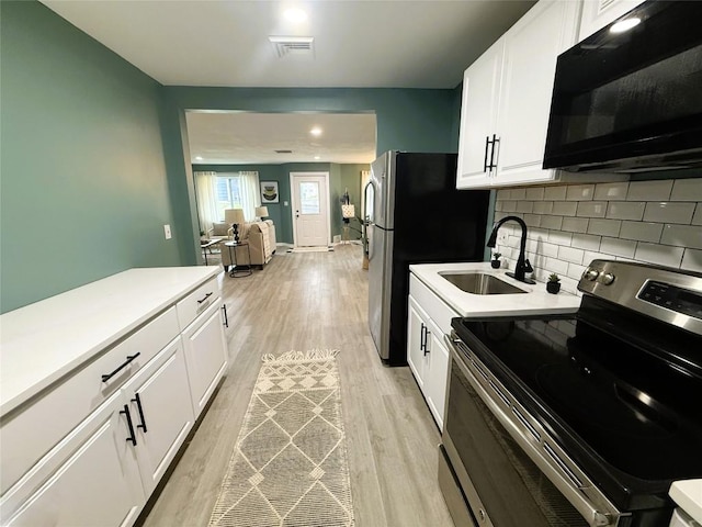 12013 Teifer Ave, Conneaut Lake, PA 16316 - kitchen with stainless steel appliances, a sink, light wood-style floors, white cabinetry, and tasteful backsplash