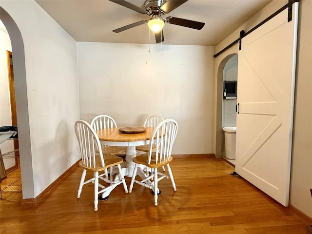 dining area featuring a barn door, ceiling fan, and light hardwood / wood-style floors