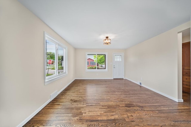 empty room featuring dark wood-style flooring, baseboards, and a chandelier