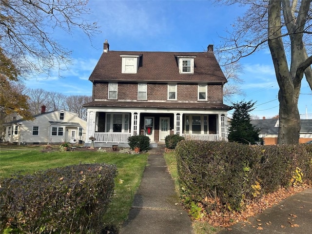 view of front of home featuring a front yard, covered porch, brick siding, and a chimney