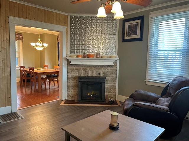 living room featuring wood-type flooring, ceiling fan with notable chandelier, a brick fireplace, and crown molding