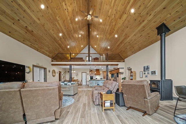 living room with ceiling fan, a wood stove, high vaulted ceiling, and light hardwood / wood-style flooring