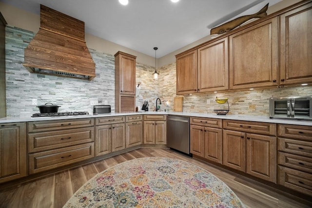 kitchen with hanging light fixtures, stainless steel appliances, backsplash, hardwood / wood-style floors, and custom range hood