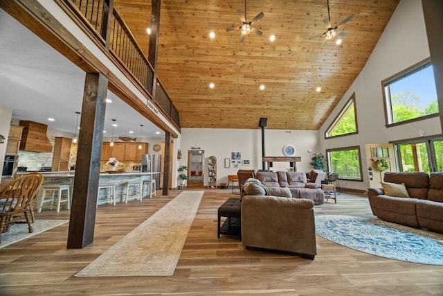 living room with wooden ceiling, a wood stove, high vaulted ceiling, and light hardwood / wood-style flooring