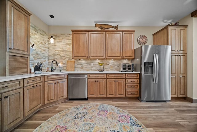 kitchen featuring sink, hanging light fixtures, stainless steel appliances, tasteful backsplash, and light hardwood / wood-style flooring