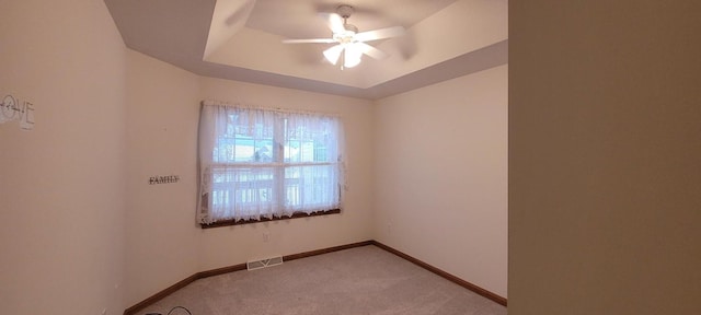 empty room with carpet, ceiling fan, and a raised ceiling