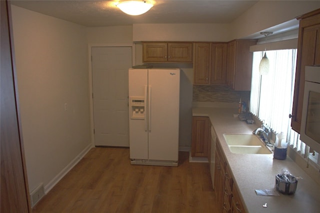 kitchen featuring light hardwood / wood-style floors, decorative backsplash, white appliances, pendant lighting, and sink