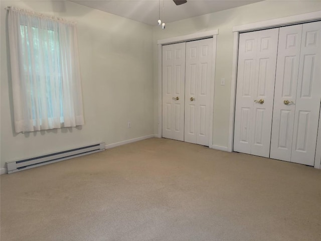 unfurnished bedroom with ceiling fan, light colored carpet, baseboard heating, and multiple closets