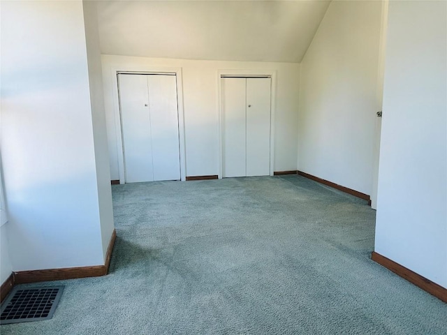 unfurnished bedroom featuring carpet flooring, lofted ceiling, and multiple closets