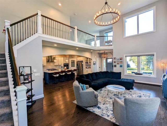 living room with a towering ceiling, dark hardwood / wood-style floors, a healthy amount of sunlight, and a notable chandelier