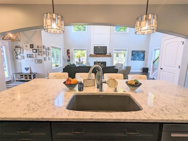 kitchen featuring a center island with sink, decorative light fixtures, light stone counters, and sink