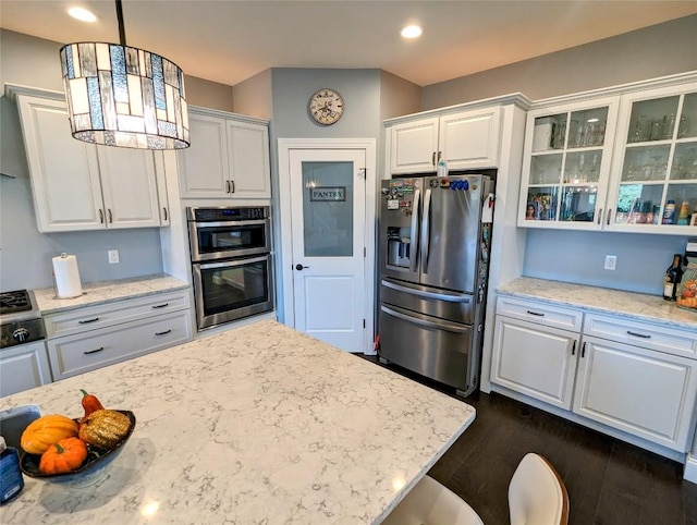 kitchen with hanging light fixtures, light stone countertops, appliances with stainless steel finishes, dark hardwood / wood-style flooring, and white cabinetry