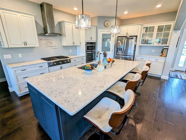 kitchen with an island with sink, hanging light fixtures, wall chimney exhaust hood, and stainless steel appliances