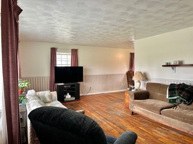 living room featuring a wainscoted wall, a textured ceiling, and wood finished floors